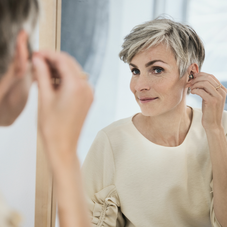 women inserting invisible hearing aid into her ear